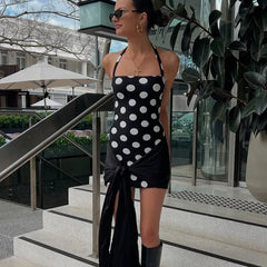Woman in a black and white polka dot dress standing outdoors near steps and plants.
