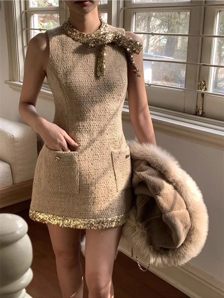 Person wearing a beige dress with decorative elements, holding a fur coat indoors.
