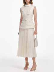 Woman wearing a sleeveless beige top and pleated skirt with a white handbag on a white background
