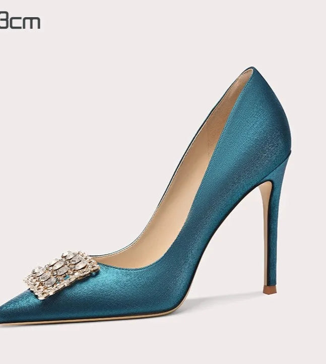 Teal high-heeled shoe with decorative brooch on a white background