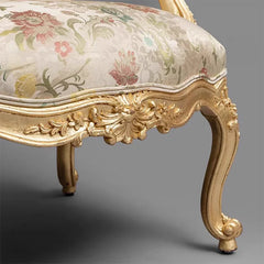 Decorative chair with floral patterned fabric and gold ornate frame on a gray background