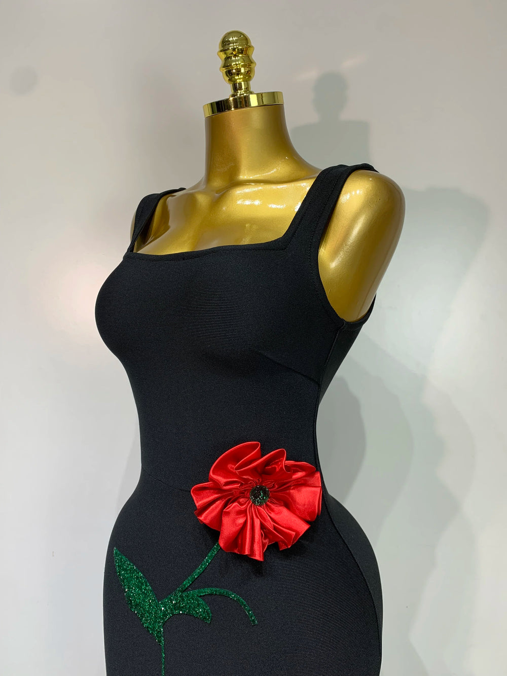 Close-up of the bodice on a black body-skimming gown showcasing a red floral appliqué.