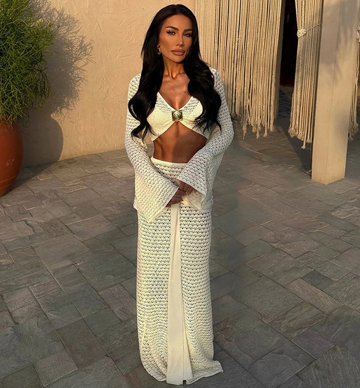 Woman in a white textured dress standing outdoors with a plant and draped fabric in the background.