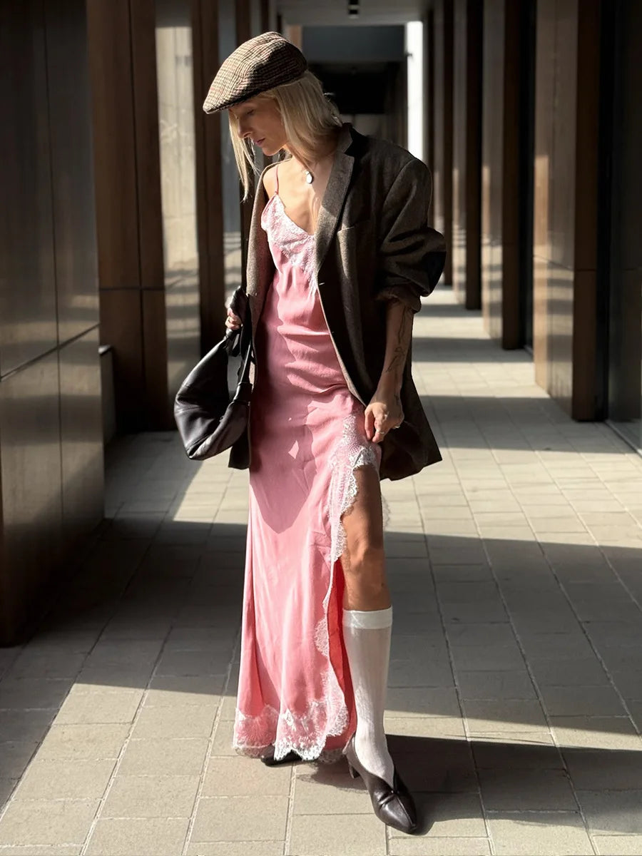 Woman in a pink dress and white boots standing in a sunlit outdoor area.