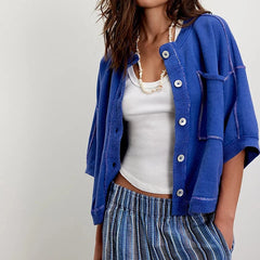 Woman wearing a blue cardigan over a white top and striped pants on a plain background