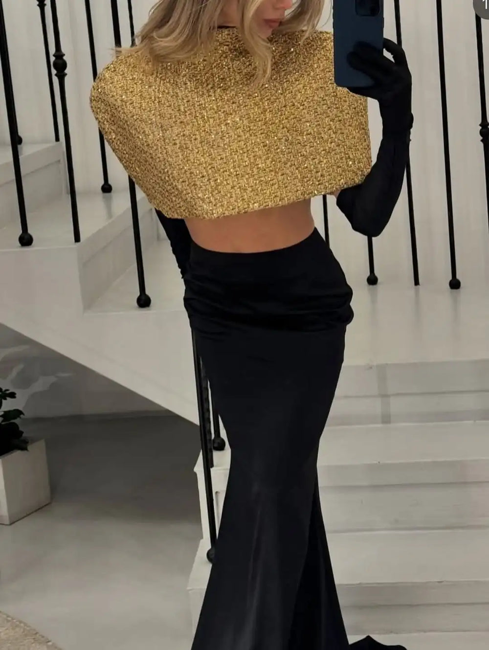 Person wearing a gold top and black skirt with gloves, standing on a staircase.