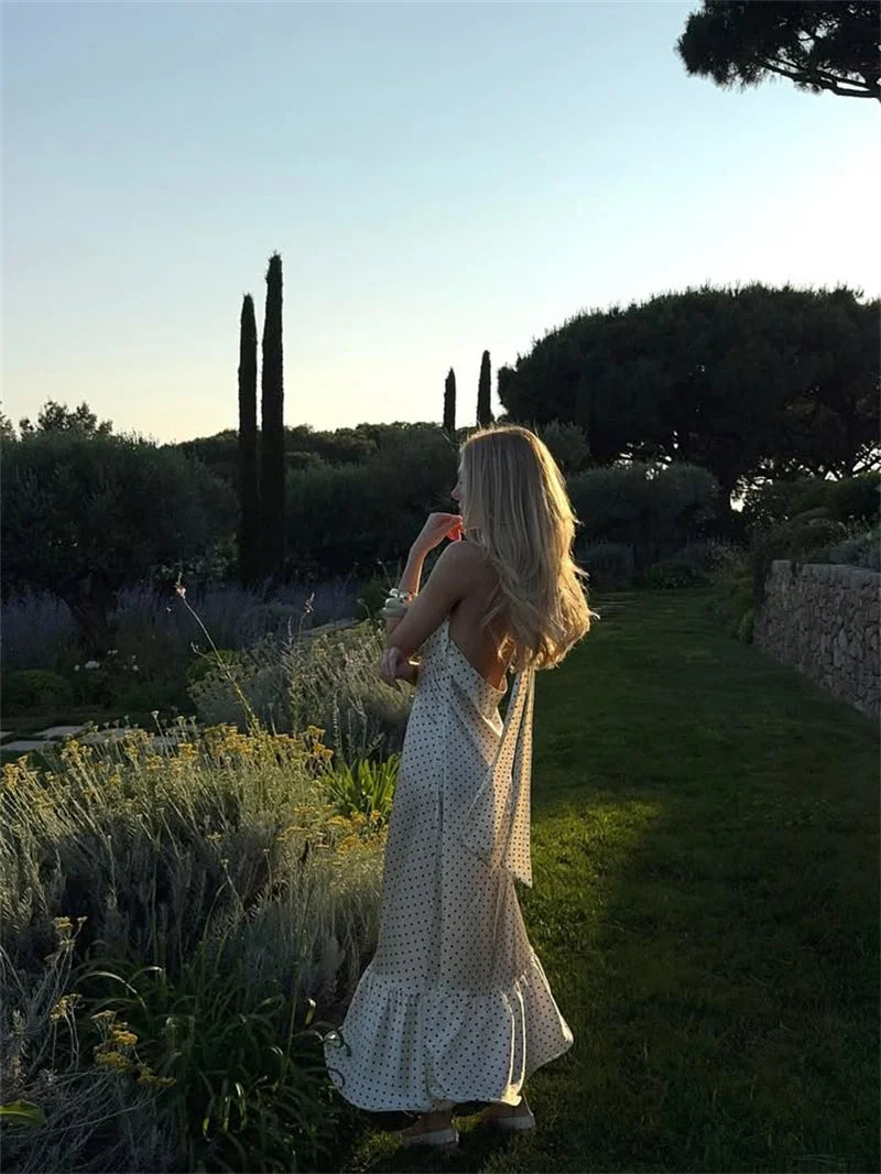 Woman in a white dress standing in a garden with trees and plants around.