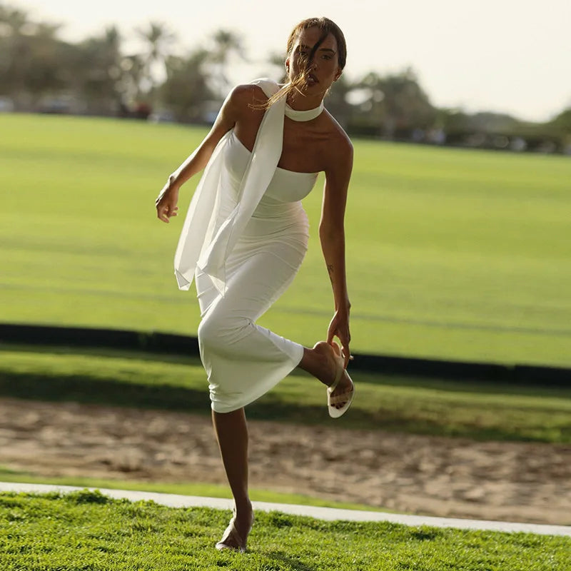 Woman in a white dress standing on a grassy field with trees in the background