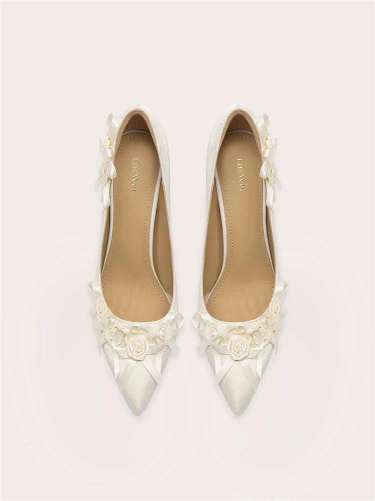 Pair of white pointed-toe shoes with floral embellishments on a light gray background