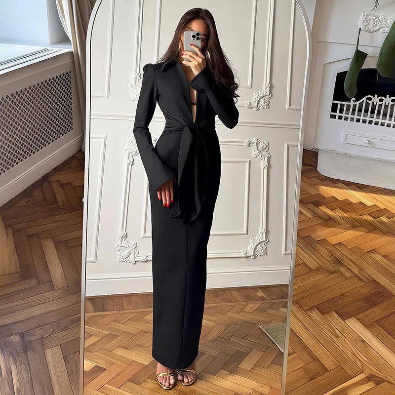 Woman taking a mirror selfie wearing a black suit in a room with wooden flooring and white walls.