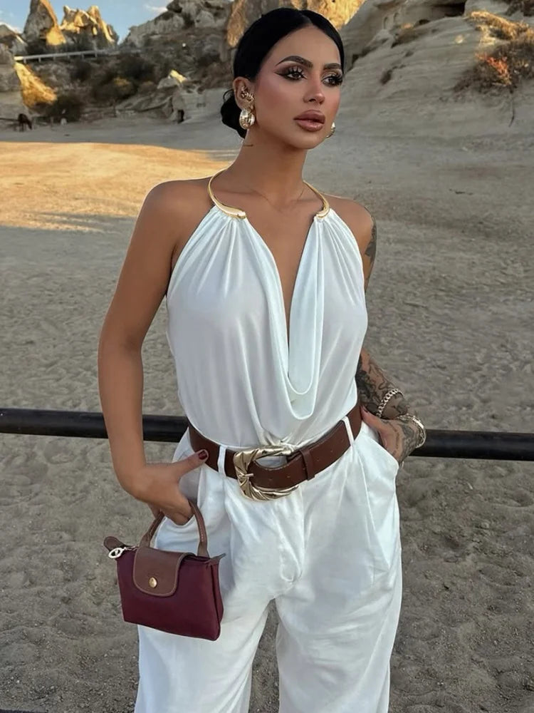 Woman in a white outfit with a brown belt and red handbag standing on a sandy beach.