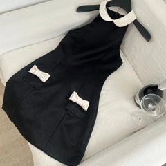 Black satin halter neck mini dress with white collar and white bow pockets on a hanger