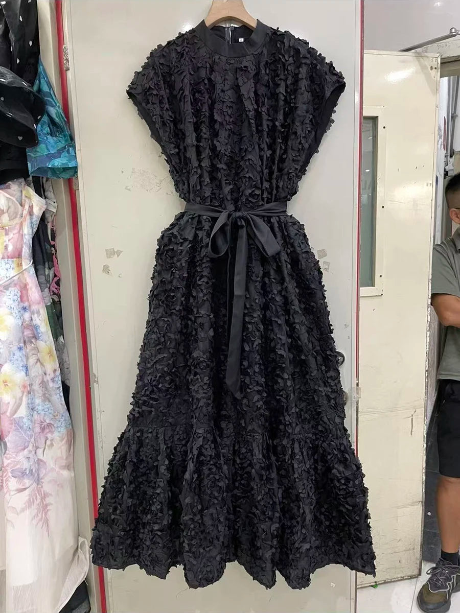 Black lace dress on a hanger against a white wall.