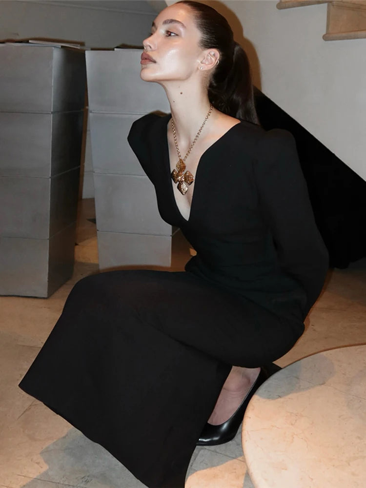 Woman in a black dress sitting on a wooden floor with a neutral background