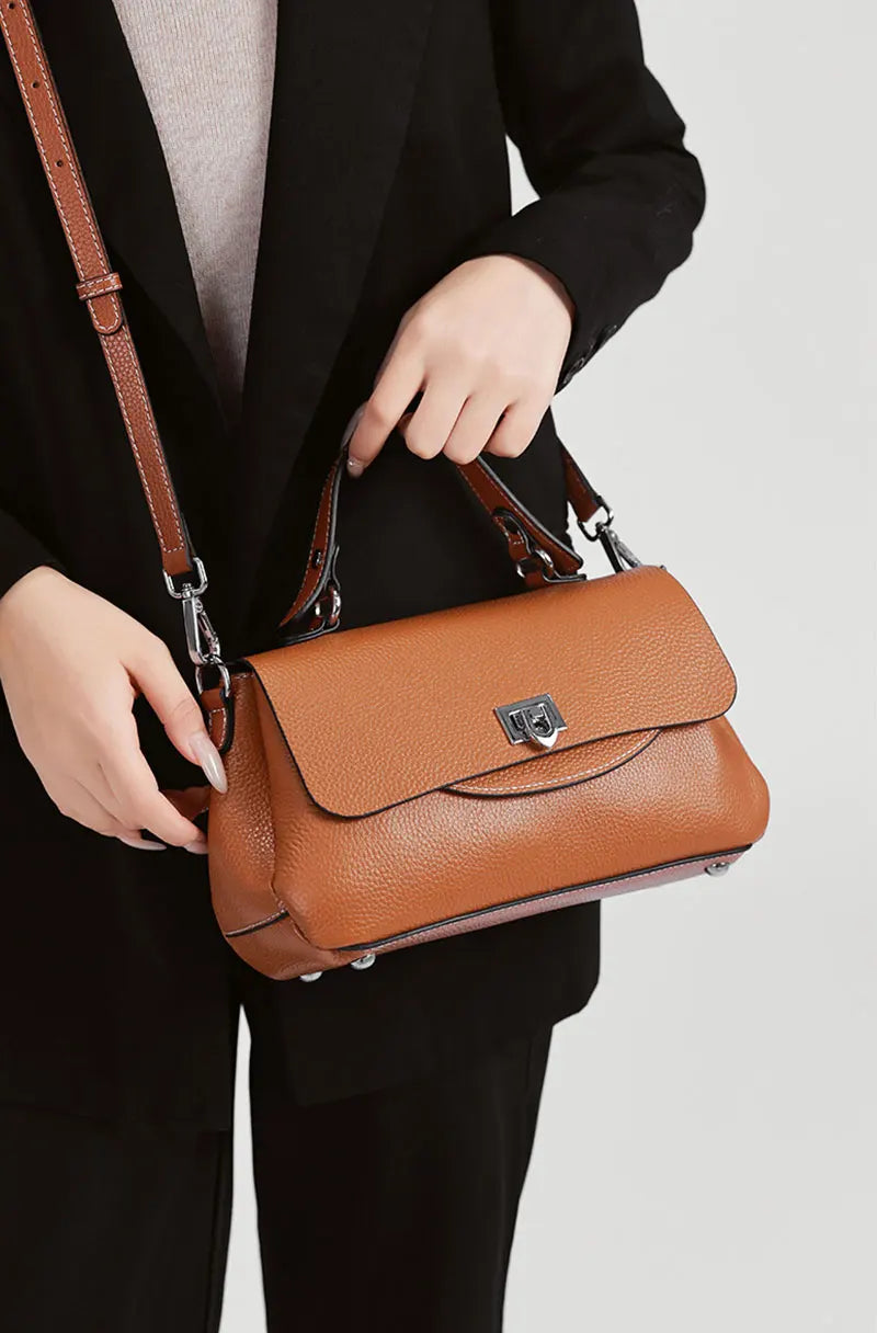 Brown handbag held by a person wearing a black suit on a white background