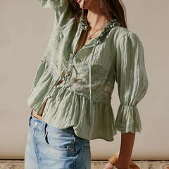 Woman wearing a light green blouse with lace details and blue jeans against a neutral background