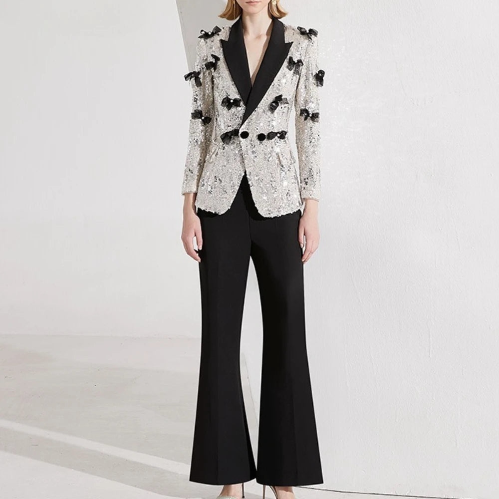 Person wearing a stylish black and white outfit with a sequined jacket on a light gray background