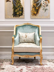 Decorative armchair with gold frame and green cushion in a room with peacock feather artworks on the wall.