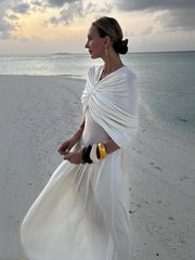 Woman in a white dress standing on a beach with ocean and sunset in the background