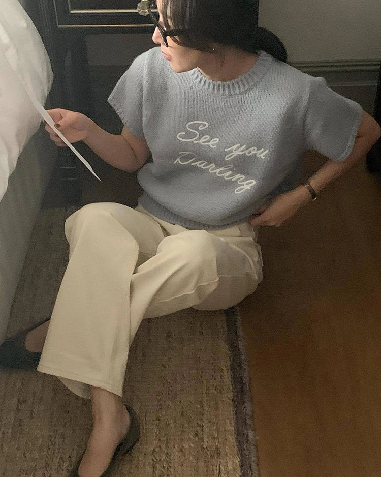Person wearing a light blue sweater with text, sitting on a bed.