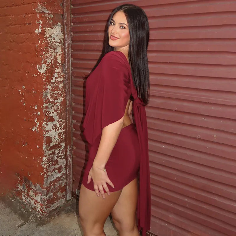 Woman in a burgundy dress standing against a red wall.