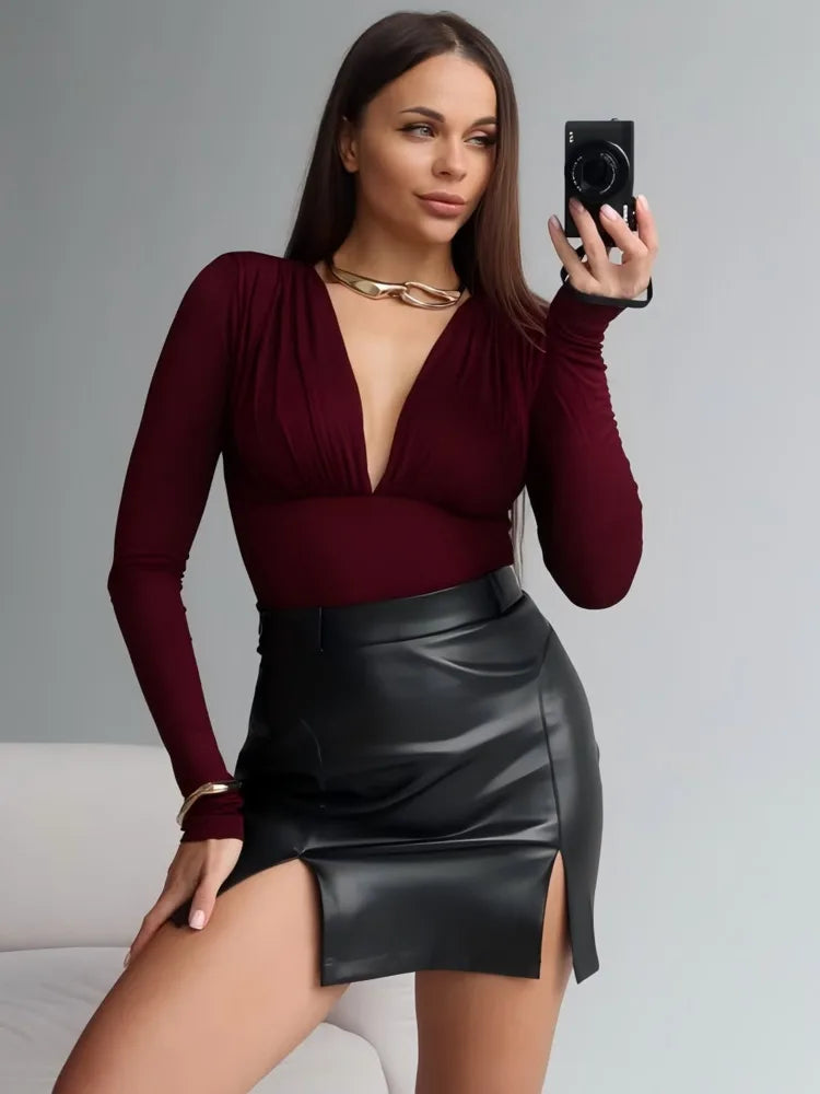 Woman taking a mirror selfie wearing a burgundy top and black leather skirt.