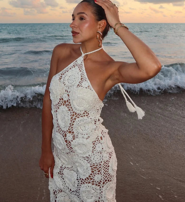 Woman in a white lace dress standing on a beach with waves in the background