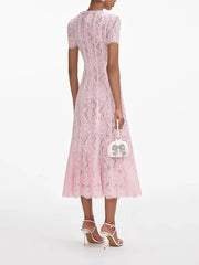 Woman wearing a pink lace dress holding a white handbag on a white background
