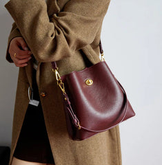 Person wearing a brown coat holding a maroon handbag with gold accents.