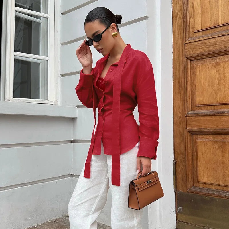 Woman wearing a red shirt and white pants standing in front of a wooden door.