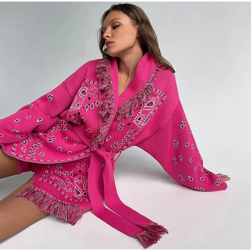 Woman wearing a bright pink scarf with paisley patterns on a plain background