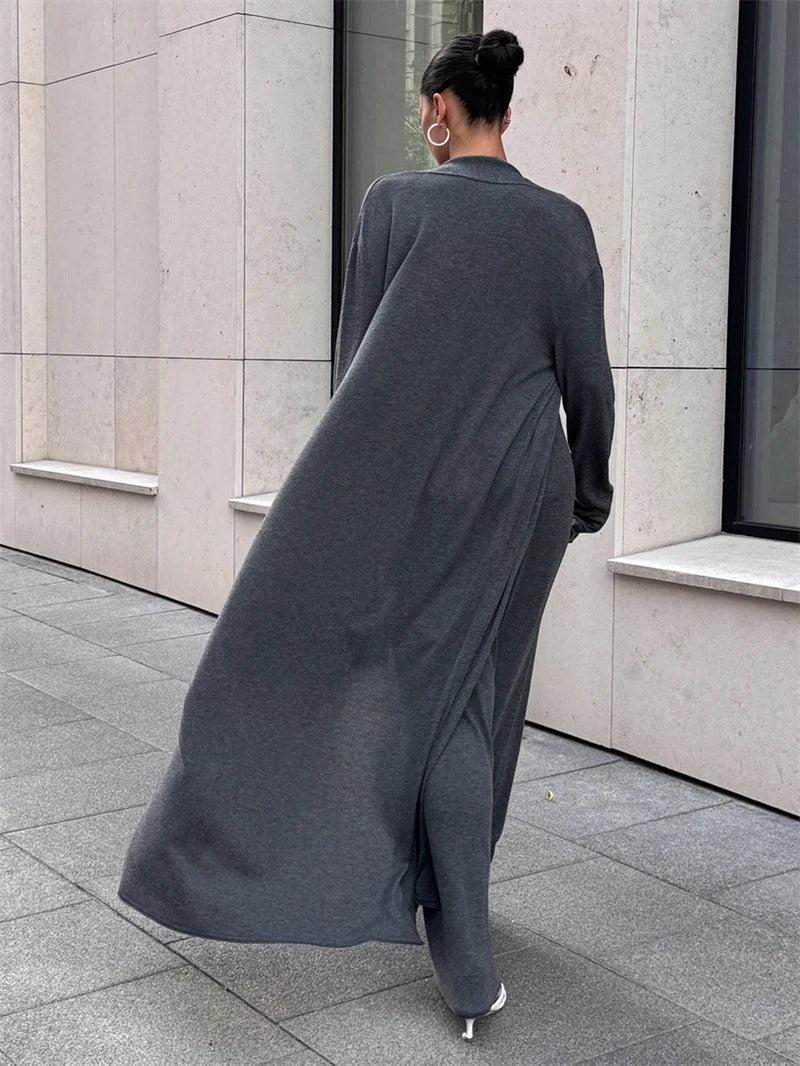 Person wearing a long dark gray dress walking on a sidewalk.