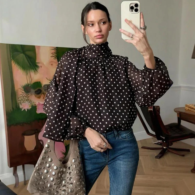 Woman taking a mirror selfie wearing a polka dot blouse and jeans in a room with furniture and decor.