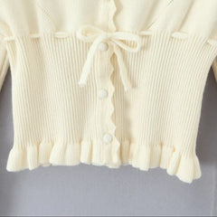 Close-up of a cream-colored knit cardigan with buttons on a light gray background