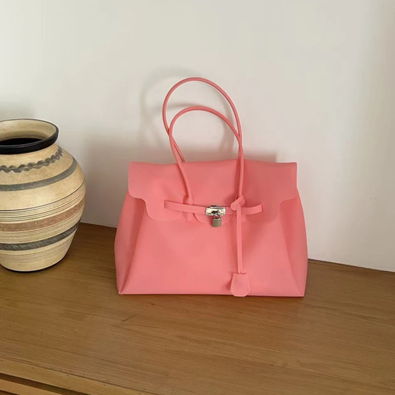 Pink structured tote bag with lock detail on a wooden surface.