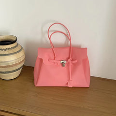 Pink structured tote bag with lock detail on a wooden surface.