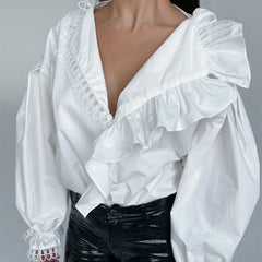 White blouse with ruffled details and a deep neckline on a gray background