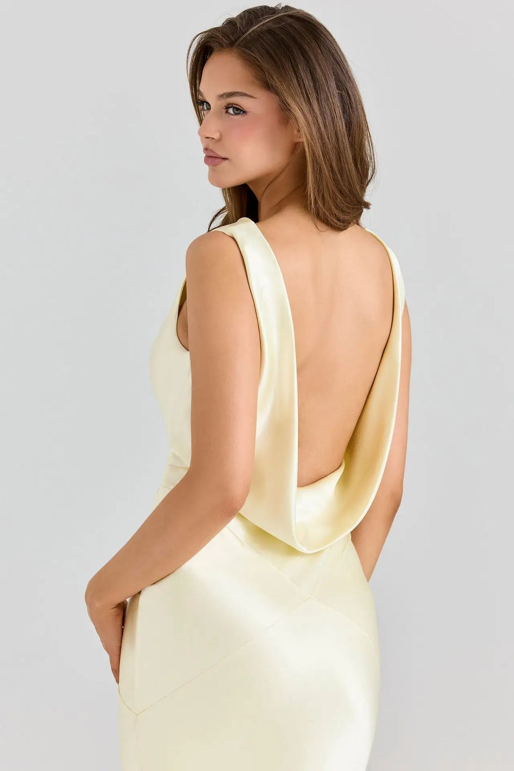 Woman wearing a light yellow dress with a backless design on a gray background