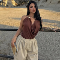 Woman in a brown top and beige pants standing in a desert-like setting.