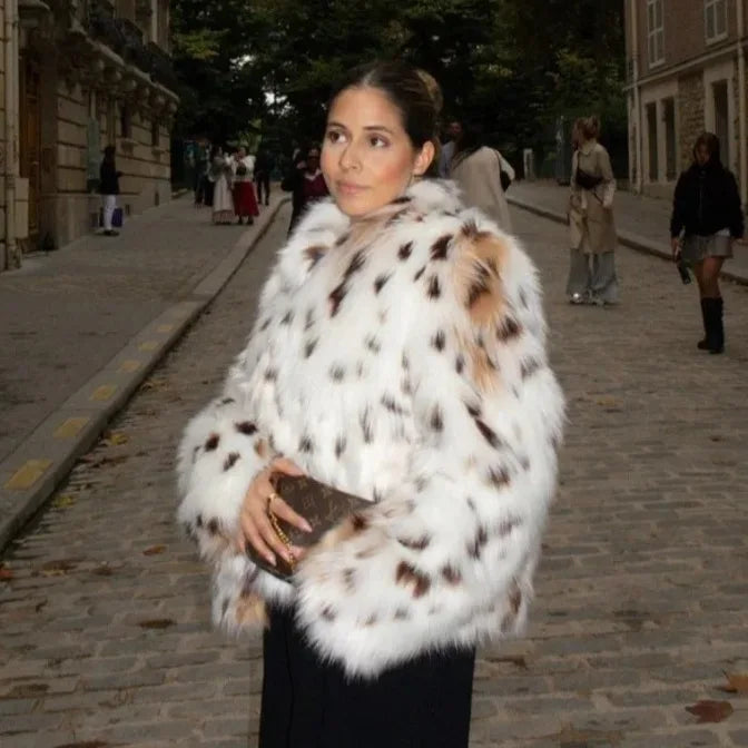 Woman wearing a white fur coat with black and brown spots on a city street.