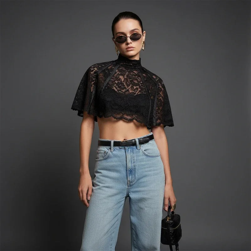 Woman wearing a black lace top and blue jeans against a gray background