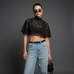 Woman wearing a black lace top and blue jeans against a gray background