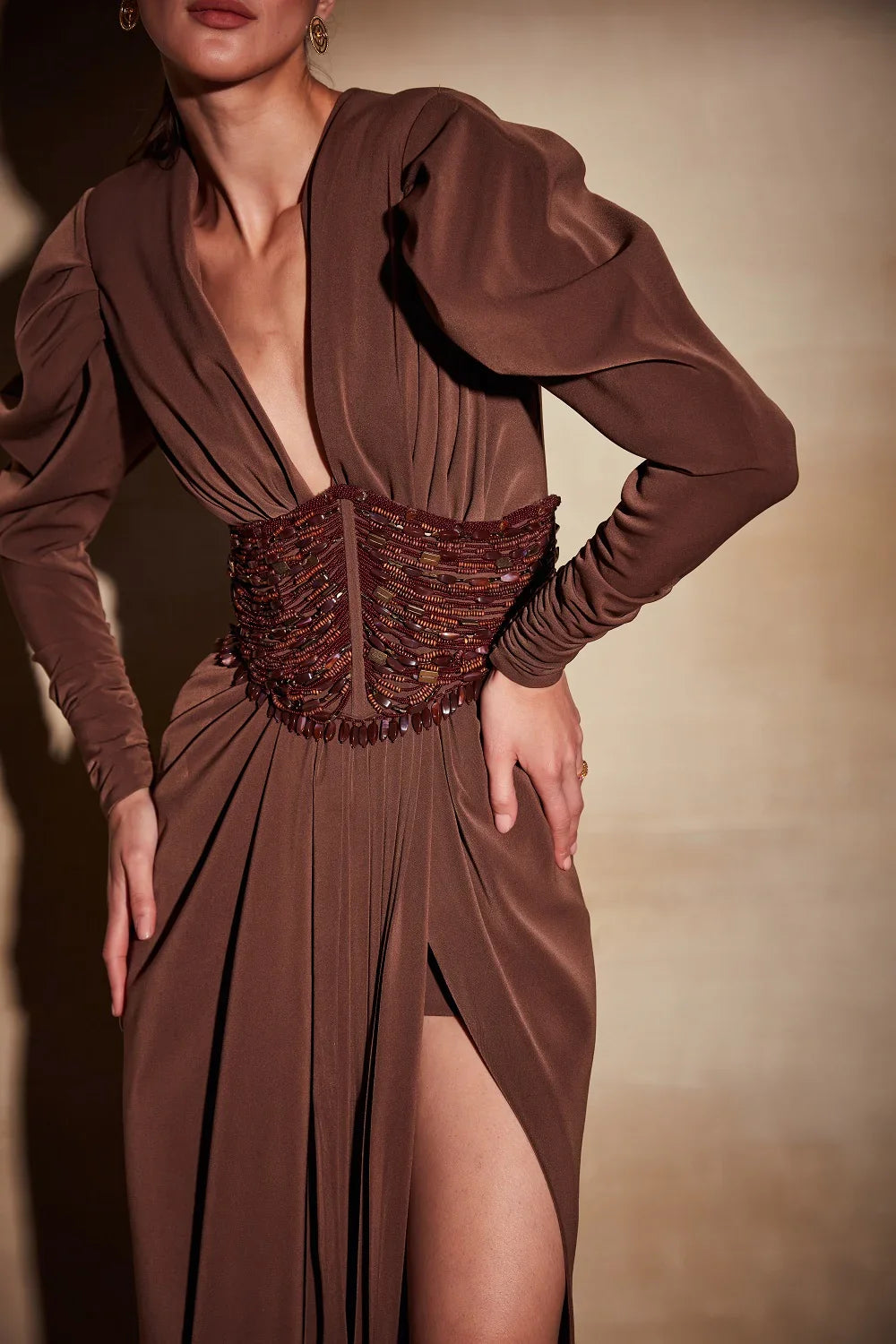 Brown evening gown with a deep neckline and slit skirt on a model against a neutral background