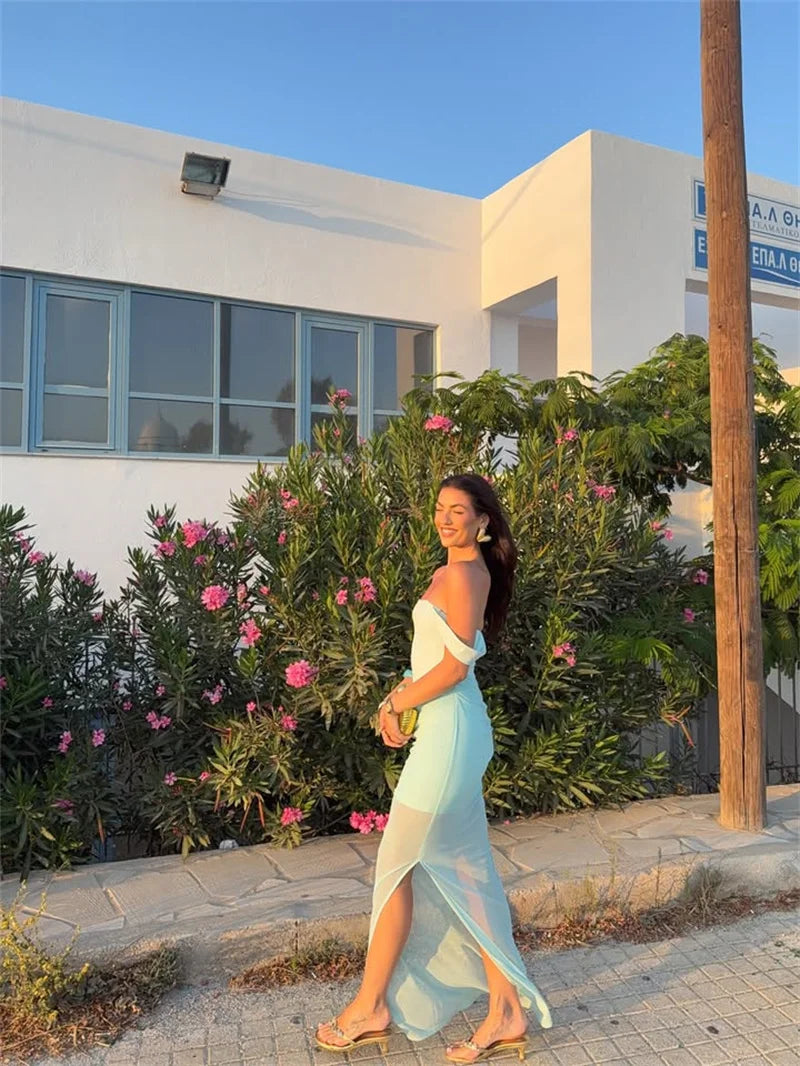 Woman in a light blue dress standing in front of a building with greenery and flowers.
