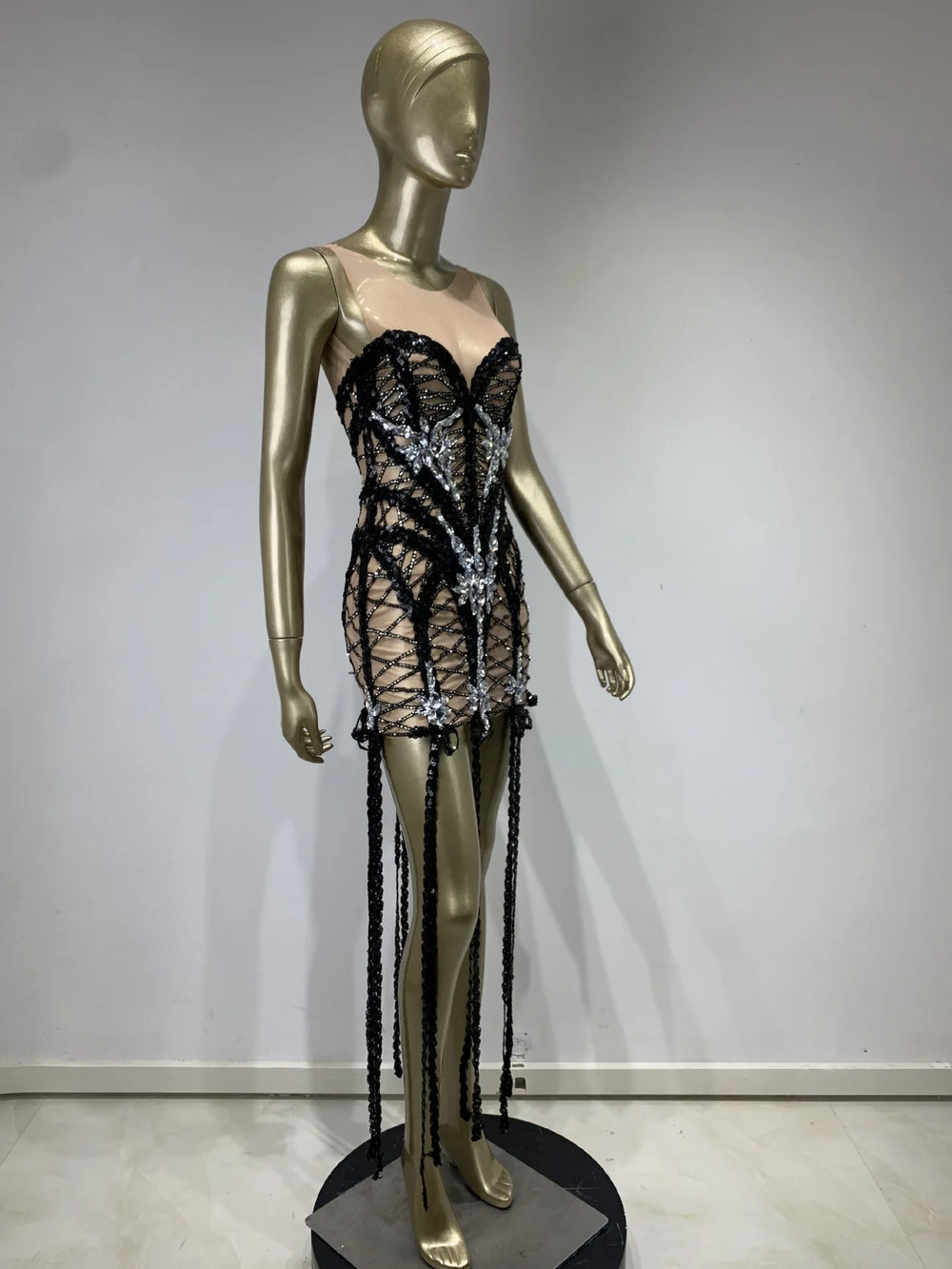 Mannequin wearing a black lace dress with long black tassels on a plain background