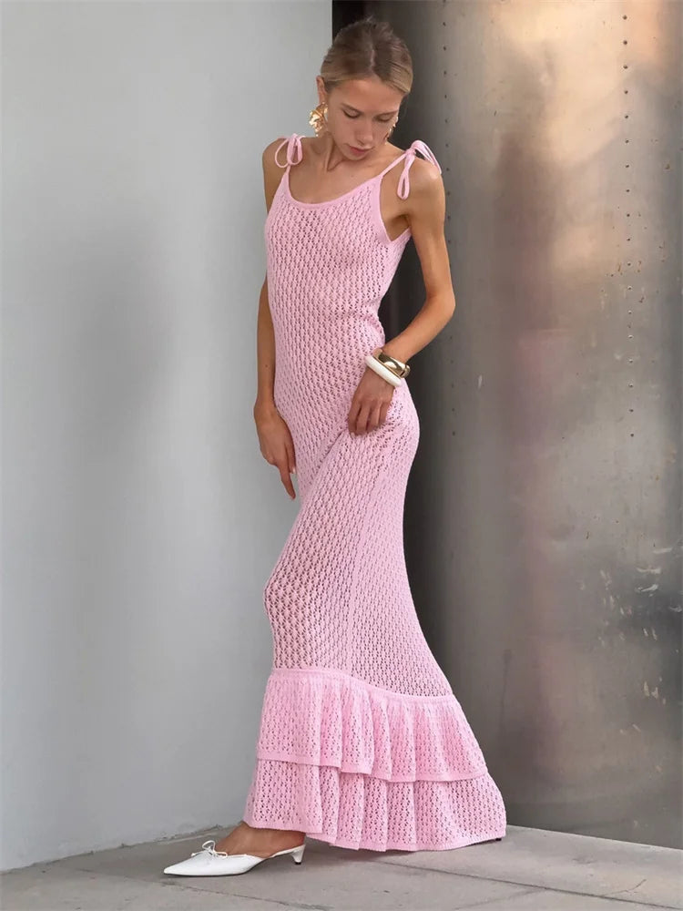 Woman wearing a pink crochet dress against a gray wall.