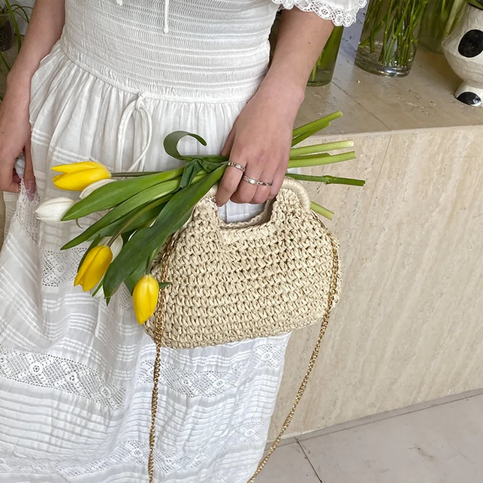 Person holding a straw bag with yellow tulips, wearing a white dress.