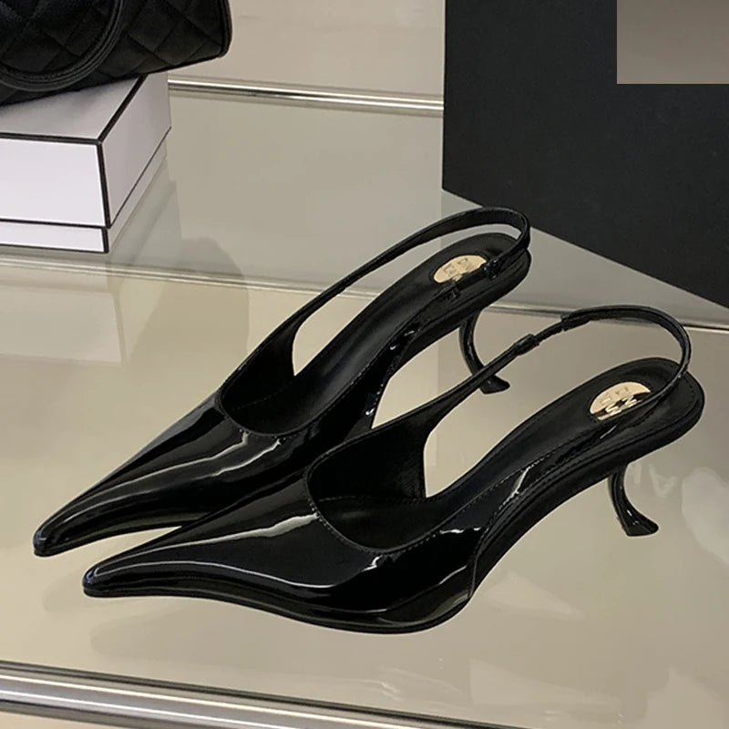 Black heeled shoes with a glossy finish on a reflective surface.