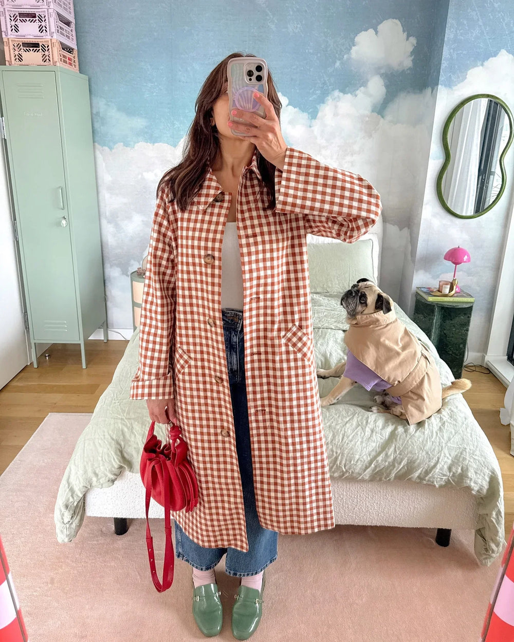Person wearing a red and white checkered coat in a room with a dog on a bed.