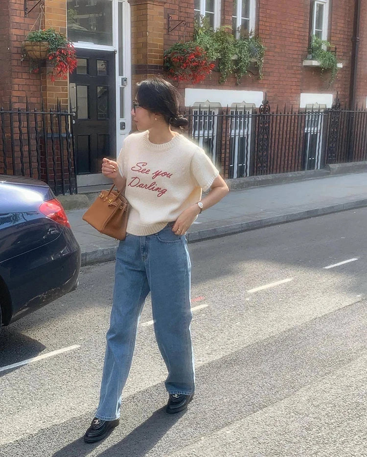 Person wearing a white t-shirt with text and blue jeans standing on a street.